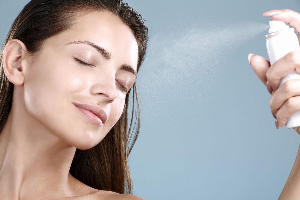26170435 - beautiful woman applying spray  water treatment on face on blue wall