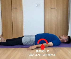 仰向けに寝転がり、腰を反らせて腰と床の間にスペースを作ります。この体制がツライと感じる方は、クッションやタオルを腰の下に入れて調整してください
