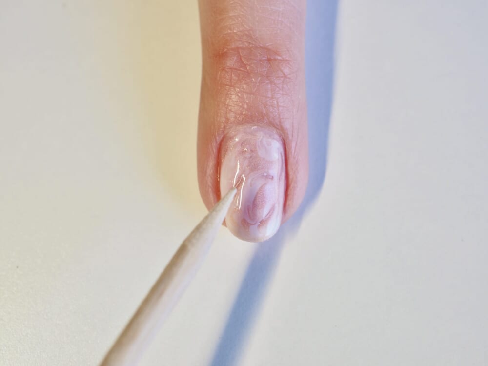 （2）が乾く前に、爪楊枝を使ってホワイトカラーのドットをマーブル模様に崩していきます。爪楊枝を動かす際は爪に強く押し当てないよう、カラーの表面の部分を滑らすように動かしてください